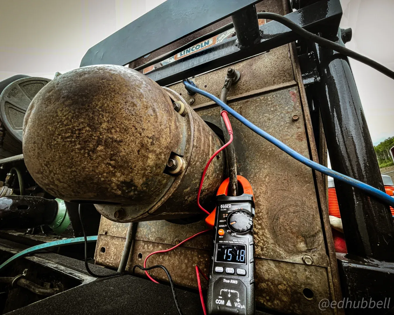 Field inspection set-up with a multimeter clipped to equipment beside a corroded steel cylinder
