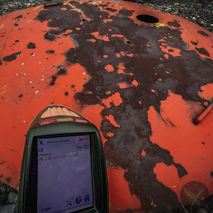 Handheld XRF analyzer testing a weathered orange painted steel surface